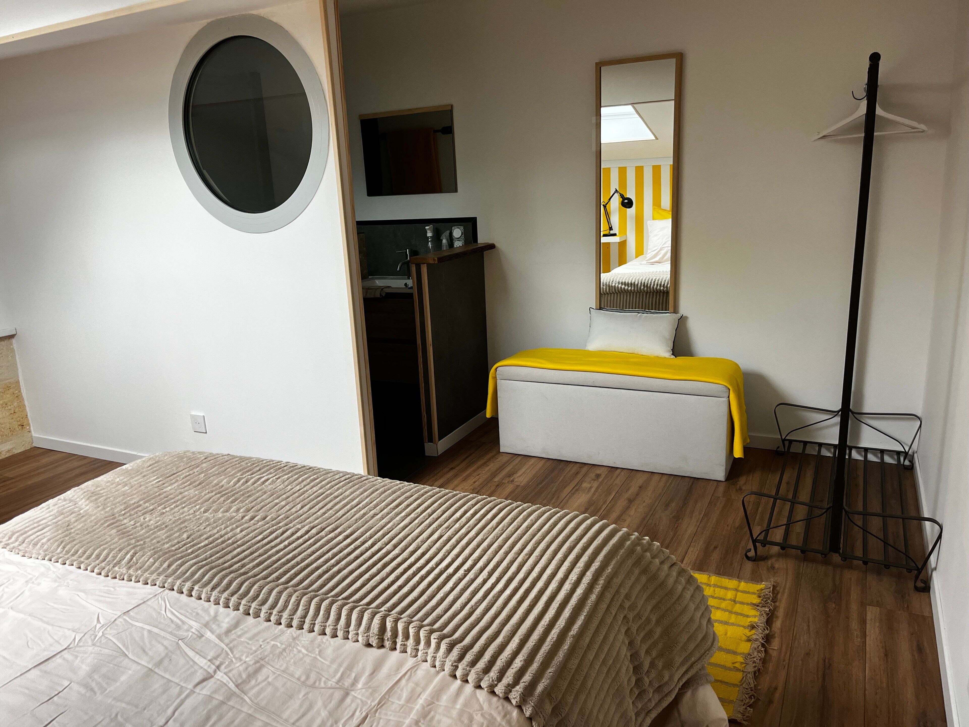 Un dormitorio con cama, una kitchenette pequeña, un espejo y una lámpara de pie.