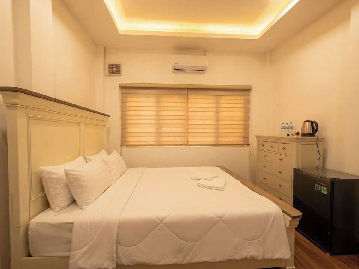 A hotel room with a bed, a dresser, a heater, and a window with blinds.