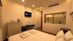 Ein Hotelzimmer mit einem Bett, einem Schreibtisch, einem Fernseher, einem Badezimmer mit Spiegel und einem an der Wand befestigten Fernseher.