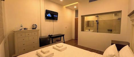 A hotel room with a bed, a TV, a desk, a mirror, and a bathroom with a shower.