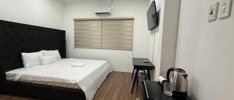 A hotel room with a bed, a desk, a TV, and a kitchenette area.