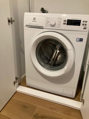 Eine kompakte, weiße Electrolux PerfectCare 600 Waschmaschine mit digitaler Bedienkonsole, befindet sich in einem kleinen Waschraum mit Holzboden.