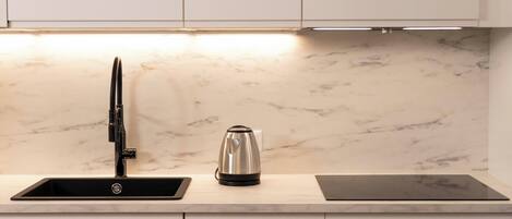 Una cocina moderna con armarios blancos, un grifo negro, una tetera y una placa de inducción negra.
