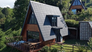 Una casa moderna con techo inclinado, terraza de madera y un ventanal grande.