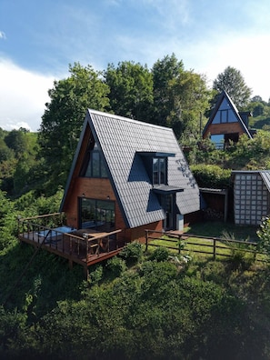 Una casa moderna con techo inclinado, terraza de madera y un ventanal grande.