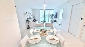 Un espace repas moderne avec une table en verre, des sets de table en fibres tressées et un arrangement floral central.