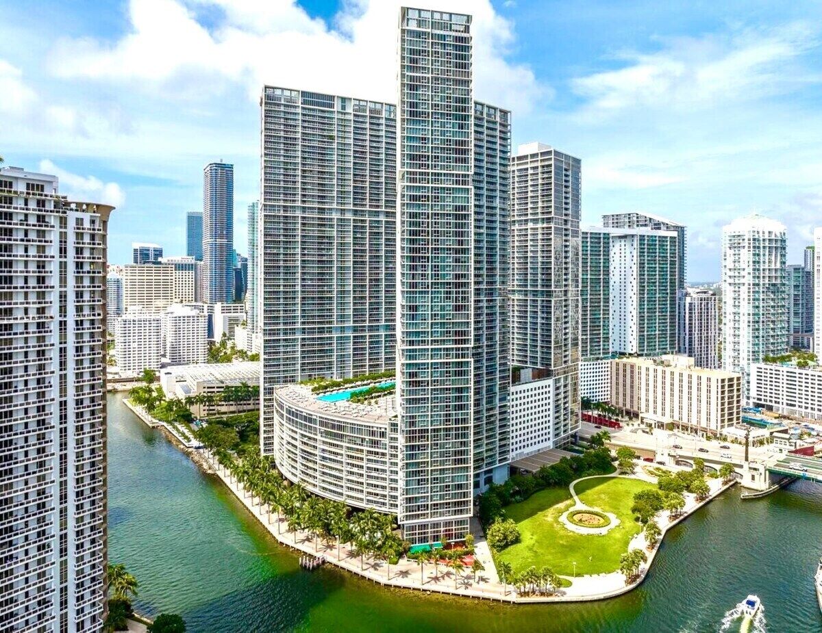A high-rise building with a curved design, surrounded by water and greenery.