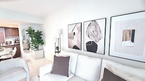Uma sala de estar moderna com um sofá branco, uma mesa de centro e uma área de jantar ao fundo.