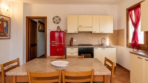 A compact kitchen with a red refrigerator, a stove, and a sink. There is a dining table with chairs and a clock on the wall. - Charming 3-bedroom Apartment in Santa Teresa Gallura (Santa Teresa di Gallura)