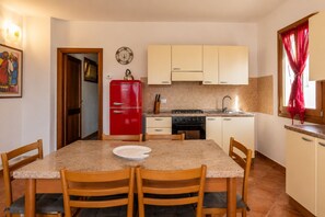 A compact kitchen with a red refrigerator, a stove, and a sink. There is a dining table with chairs and a clock on the wall. - Charming 3-bedroom Apartment in Santa Teresa Gallura (Santa Teresa di Gallura)