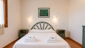 A neatly made bed with two pillows and two folded towels, a framed abstract painting above the bed, and two bedside tables with wall-mounted lamps. - Charming 3-bedroom Apartment in Santa Teresa Gallura (Santa Teresa di Gallura)