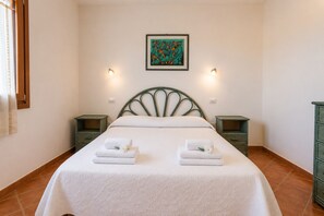 A neatly made bed with two pillows and two folded towels, a framed abstract painting above the bed, and two bedside tables with wall-mounted lamps. - Charming 3-bedroom Apartment in Santa Teresa Gallura (Santa Teresa di Gallura)