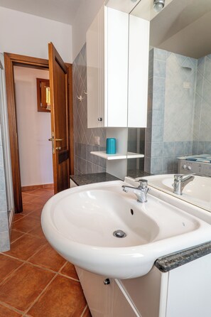A bathroom with a white sink, a mirror, and a shower area. - Charming 3-bedroom Apartment in Santa Teresa Gallura (Santa Teresa di Gallura)