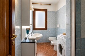 A compact bathroom with a sink, toilet, and washing machine. - Charming 3-bedroom Apartment in Santa Teresa Gallura (Santa Teresa di Gallura)