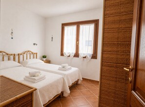 A hotel room with two beds, a small bedside table, a window with curtains, and a door. - Charming 3-bedroom Apartment in Santa Teresa Gallura (Santa Teresa di Gallura)