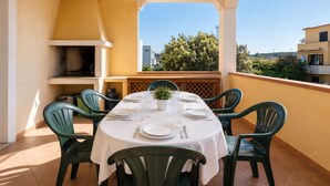 A dining area with a table set for four, surrounded by chairs, a grill, and a view of the city. - Charming 3-bedroom Apartment in Santa Teresa Gallura (Santa Teresa di Gallura)