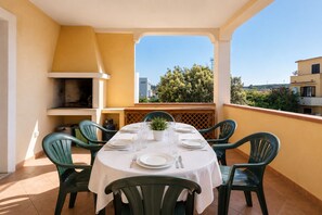 A dining area with a table set for four, surrounded by chairs, a grill, and a view of the city. - Charming 3-bedroom Apartment in Santa Teresa Gallura (Santa Teresa di Gallura)