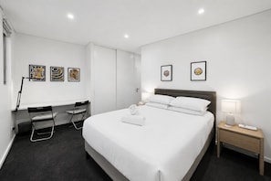 Ein Hotelzimmer mit einem Bett, einem Schreibtisch, zwei Stühlen, einem Nachttisch und Bildern an den Wänden.