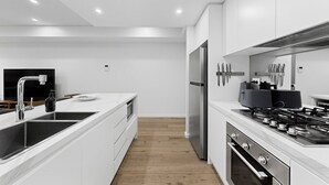 A modern kitchen with white cabinetry, stainless steel appliances, and a central island with a sink. - Designer 1-Bed Apartment with Balcony (Rozelle)