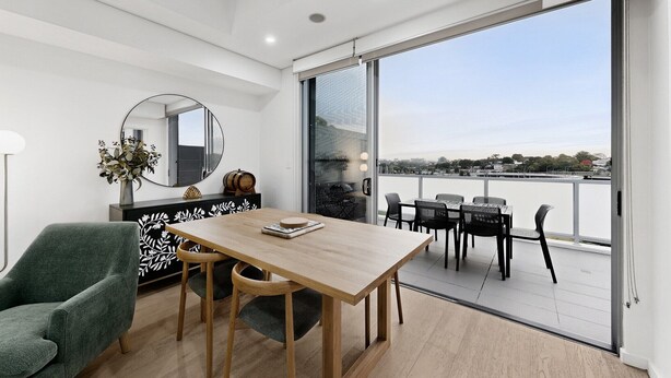A modern interior with a dining area, a green armchair, a round mirror, and a view of the outdoors. - Designer 1-Bed Apartment with Balcony (Rozelle)
