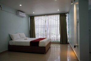 Een hotelkamer met een bed, een raam met gordijnen, een airconditioning en een betegelde vloer.