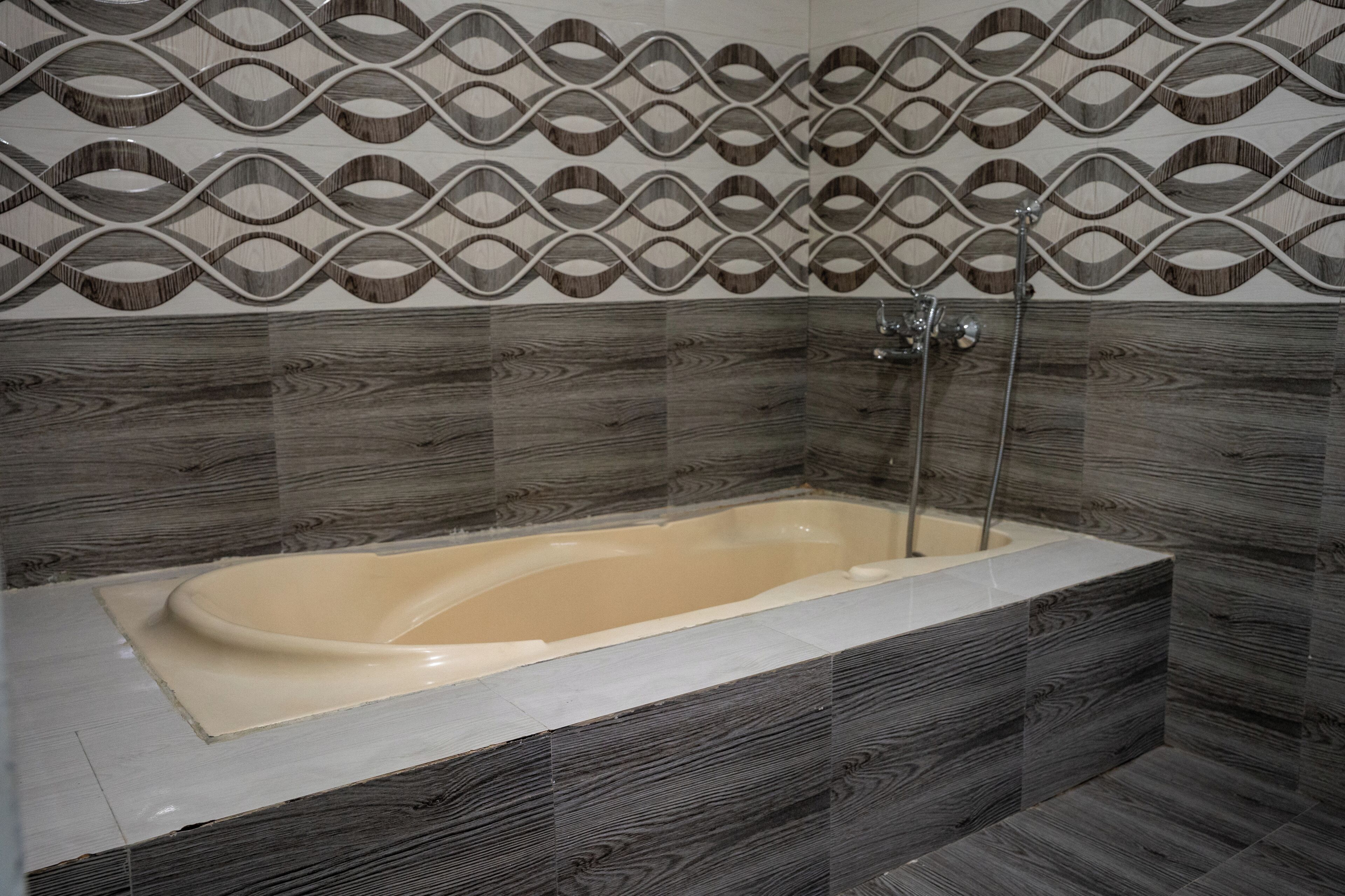 Une salle de bain avec une baignoire sur pieds, une douche et un mur recouvert de carreaux formant un motif géométrique.
