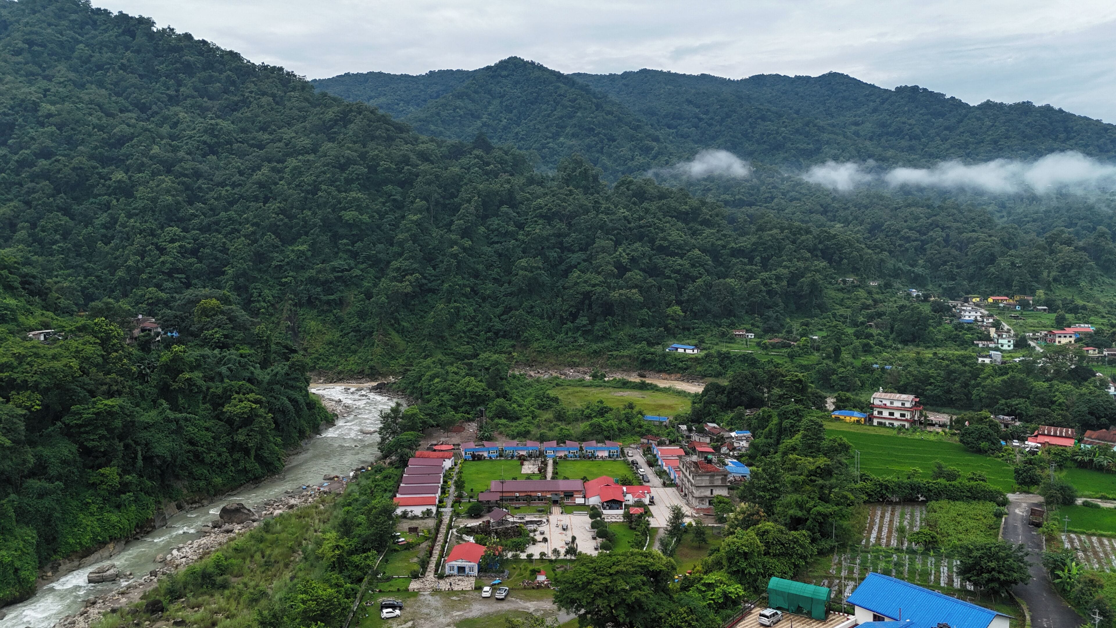 A mountainous landscape with a river, a cluster of buildings with red roofs, and lush greenery.