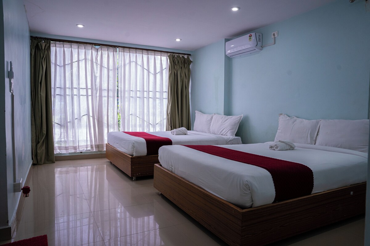 Een hotelkamer met twee bedden, een raam met dunne gordijnen en een airconditioning aan de muur.
