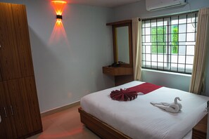 A hotel room with a bed, a bedside table, a mirror, a window with curtains, and a wall-mounted light fixture.