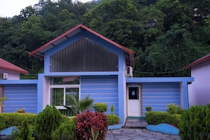A two-story building with a red roof and blue walls, surrounded by greenery.