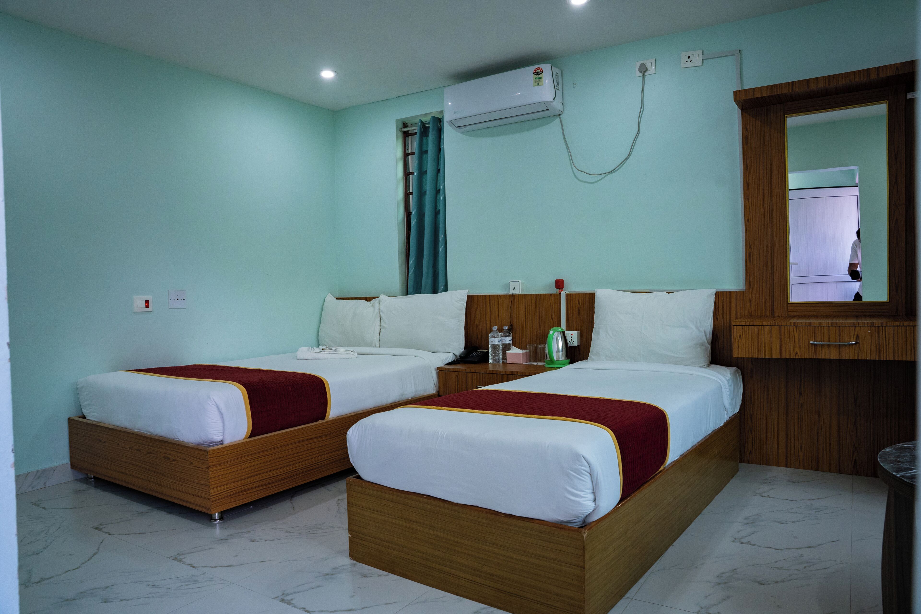Habitación de hotel con dos camas individuales, cabecero de madera, un espejo grande y un equipo de aire acondicionado.