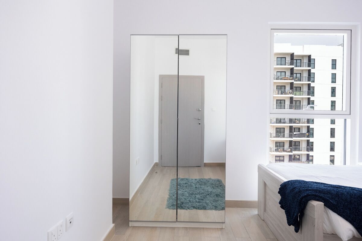 A bedroom with a bed, a wardrobe, a window, and a view of a building.