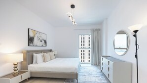 A modern bedroom with a bed, bedside table, lamp, dresser, and a large window with curtains. - Bloomfields 3BR plus maid in Waters Edge (Abu Dhabi)