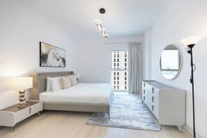 A modern bedroom with a bed, bedside table, lamp, dresser, and a large window with curtains. - Bloomfields 3BR plus maid in Waters Edge (Abu Dhabi)