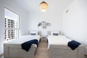 Une chambre avec deux lits, une fenêtre et un luminaire suspendu.