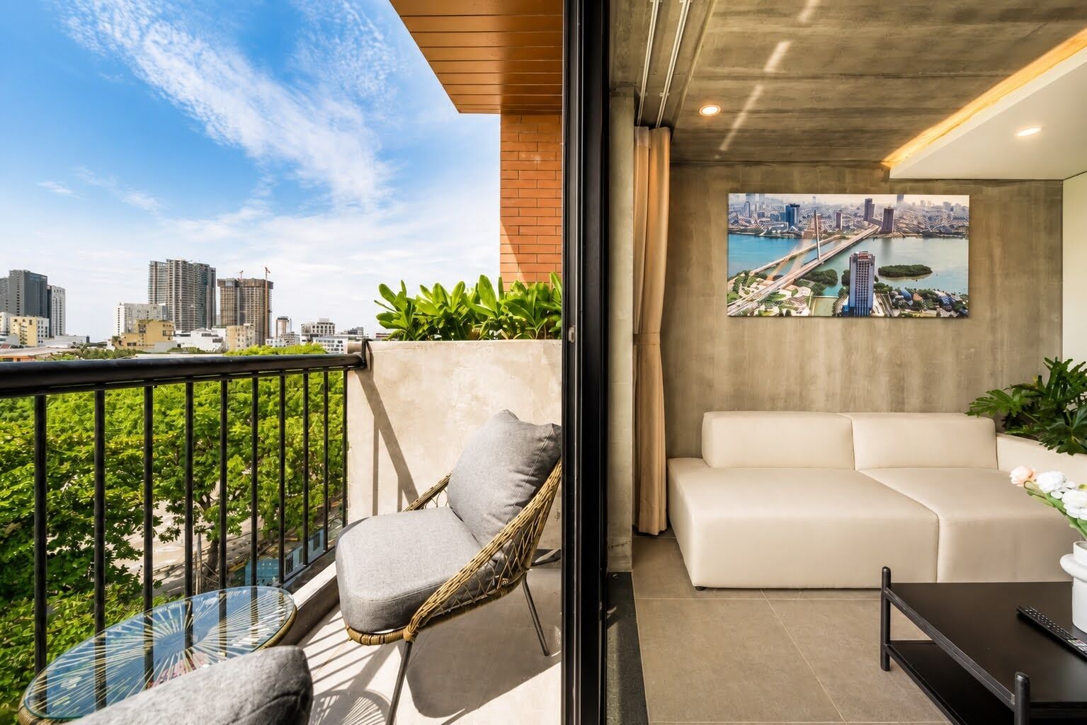 A balcony with a city view, a wicker chair, a white sofa, and a painting of a bridge.