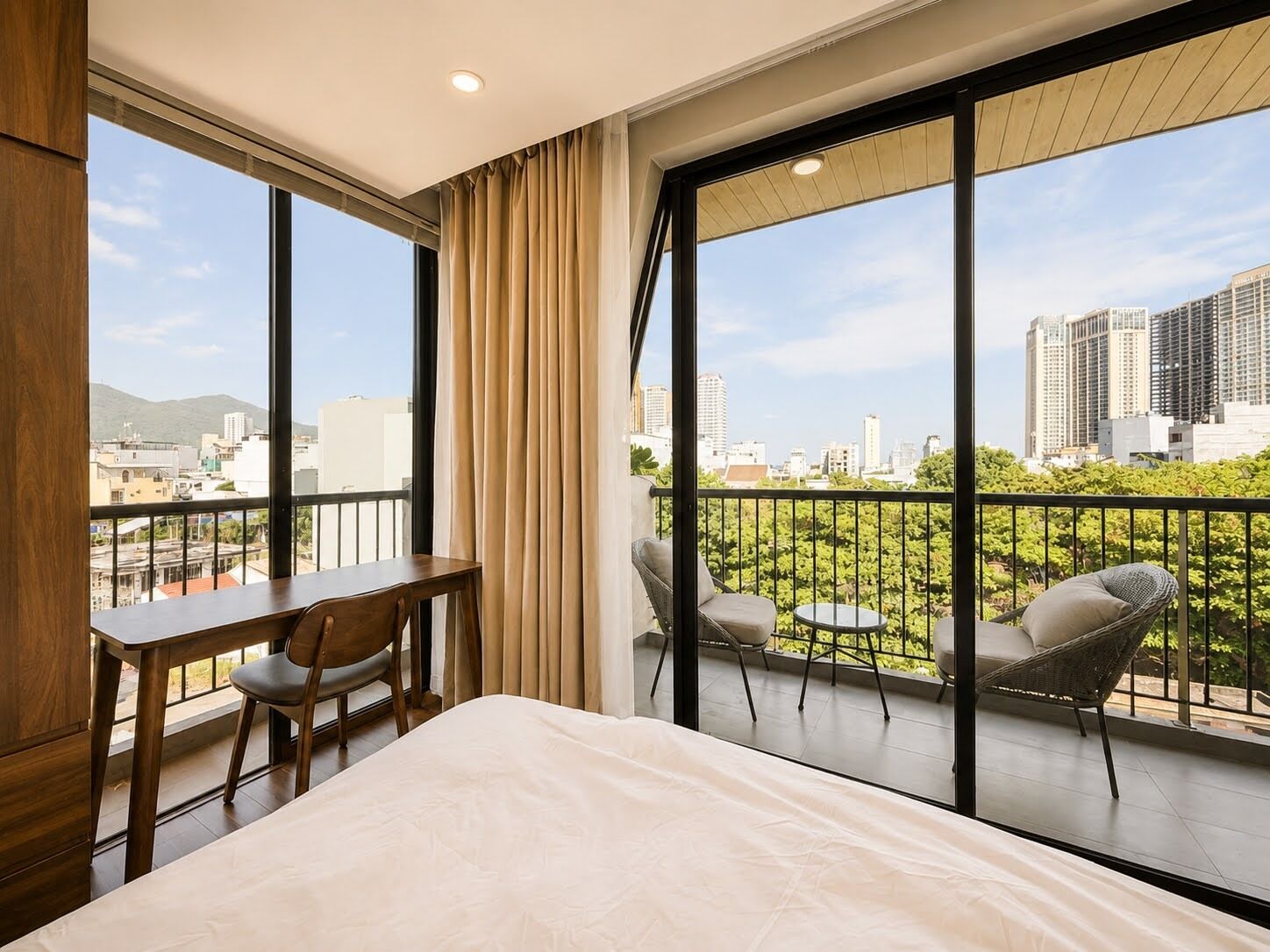 Ein Hotelzimmer mit einem großen Bett, einem Schreibtisch und einem Sessel, mit einem Balkon und Blick auf die Stadt.