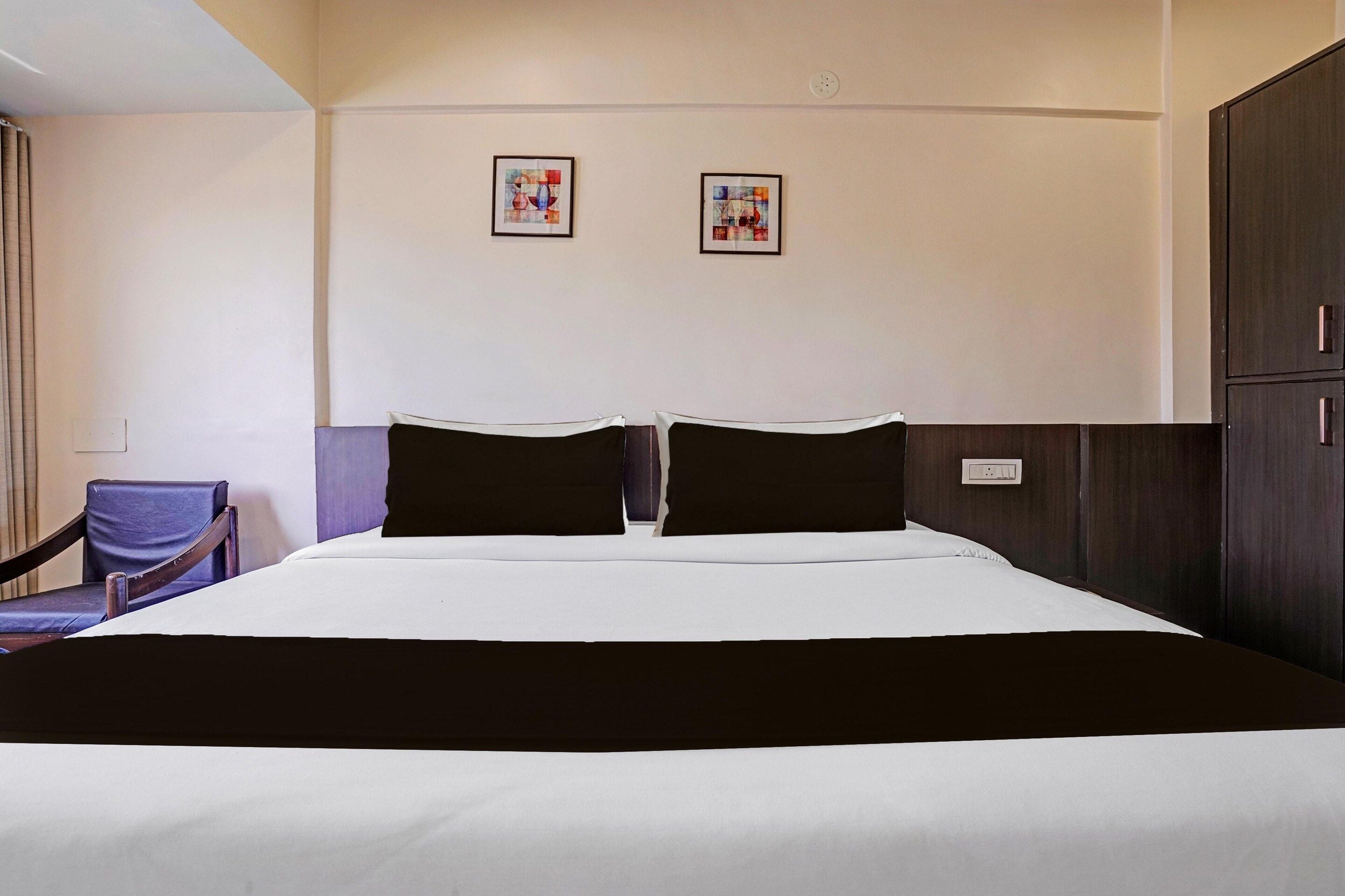 A hotel room with a bed, a chair, and two paintings on the wall.