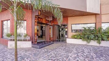A hotel entrance with a tiled patio, a white picket fence, and a palm tree.