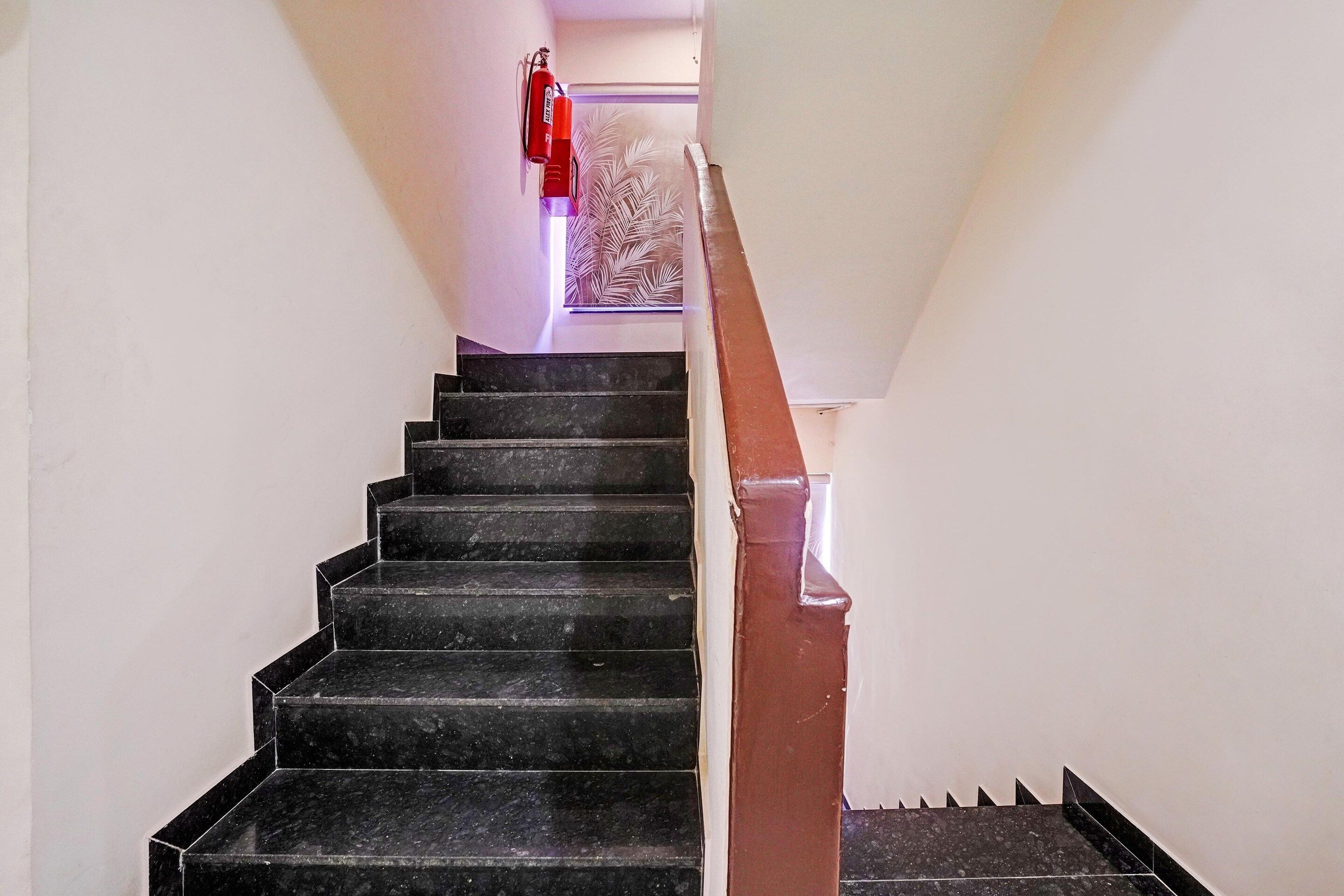 Escadaria com degraus pretos e corrimão marrom que leva a um patamar.