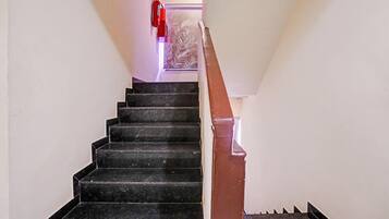 Escadaria com degraus pretos e corrimão marrom que leva a um patamar.