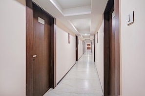 A long, narrow hallway with wooden doors on both sides and a marble floor. - Townhouse Rajkot Bus Stand (Rajkot)