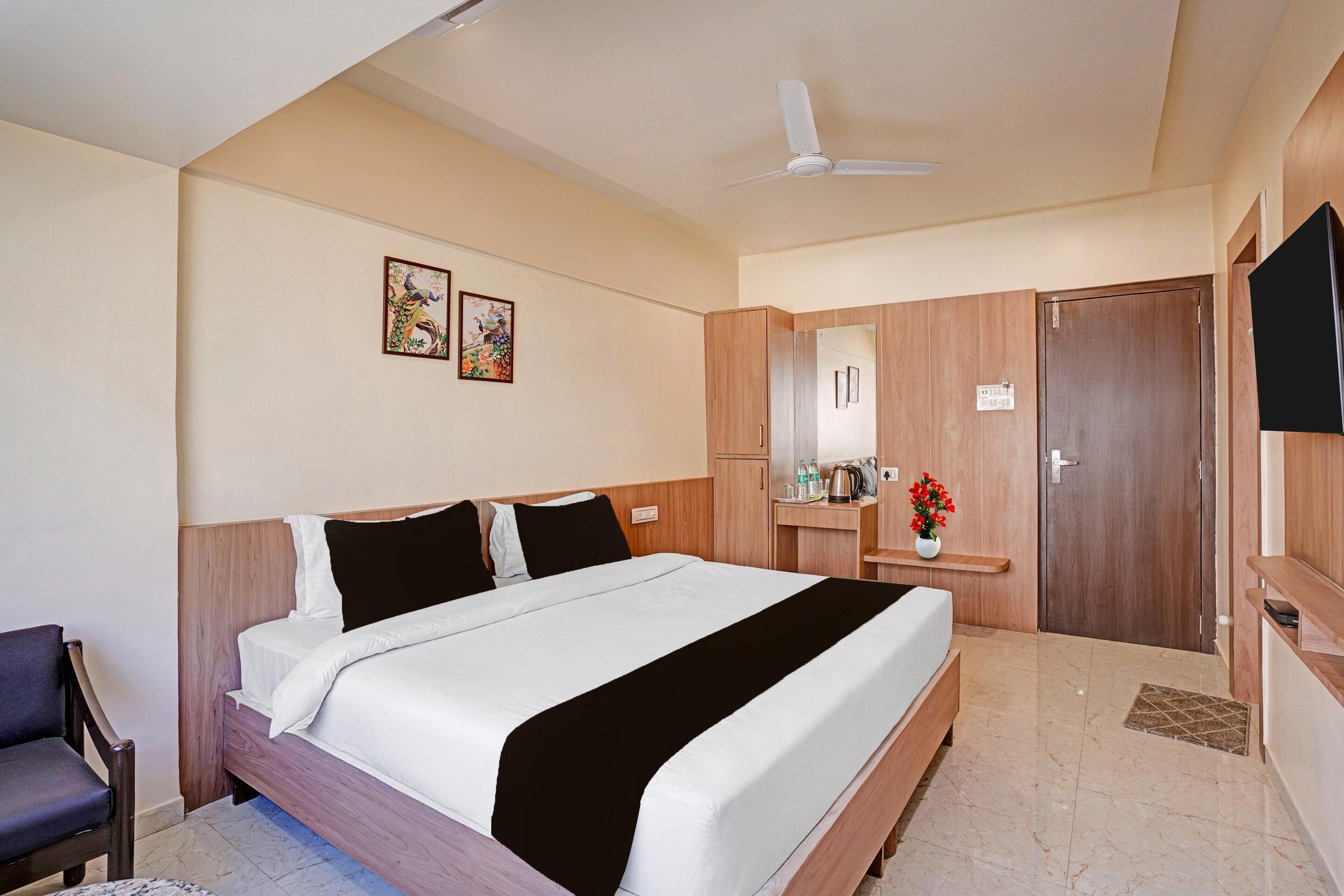 Quarto de hotel com cama, escrivaninha, cadeira, televisão e obras de arte na parede.