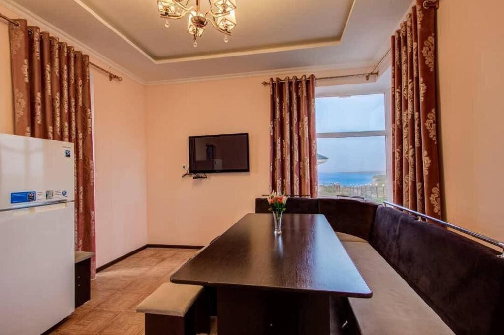 Quarto com mesa de jantar, sofá, TV na parede e janela com vista.