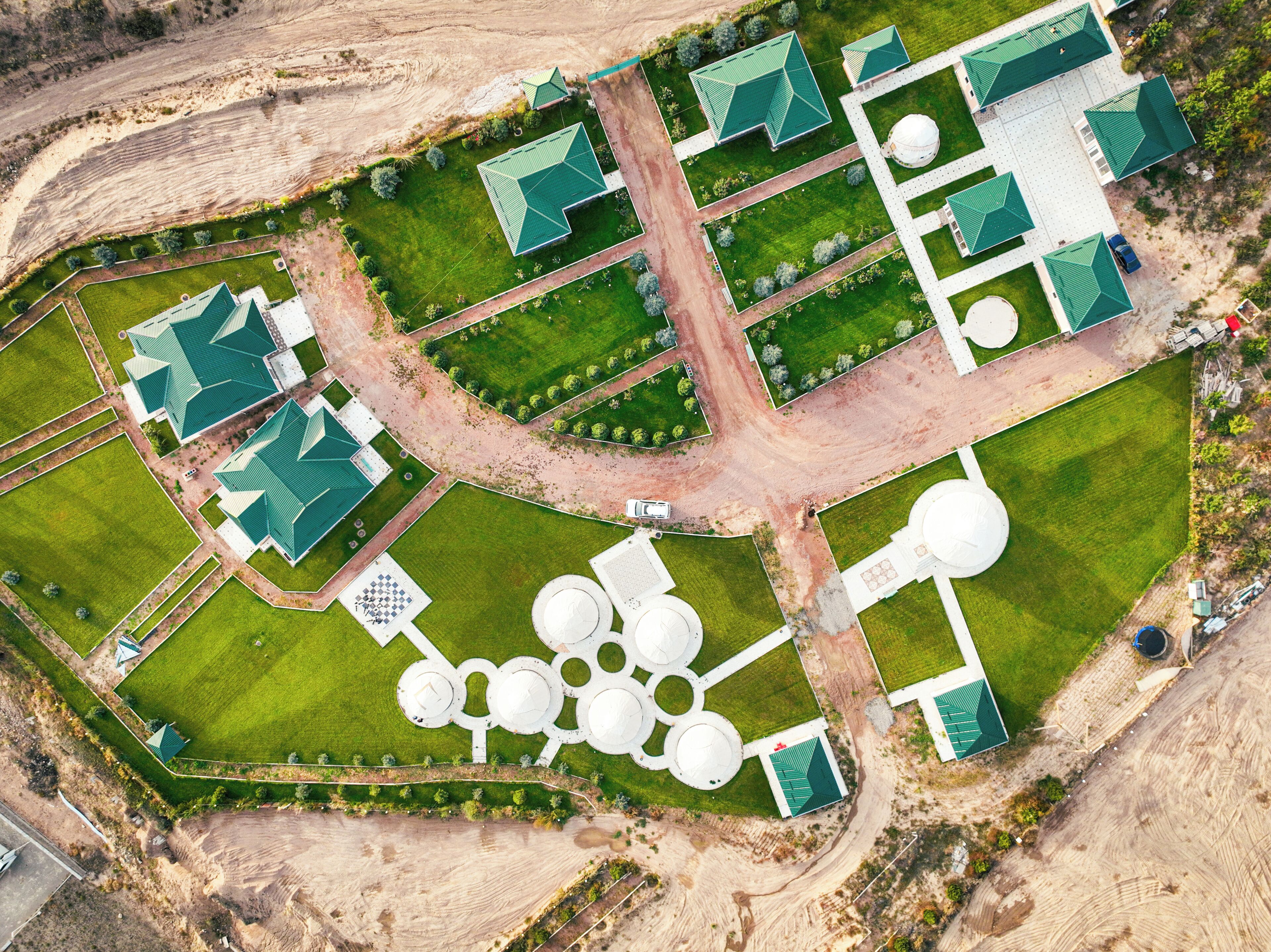 An aerial view of a property with multiple green-roofed buildings, a central circular water feature, and a well-maintained lawn.