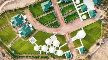 An aerial view of a property with multiple green-roofed buildings, a central circular water feature, and a well-maintained lawn.