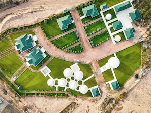 An aerial view of a property with multiple green-roofed buildings, a central circular water feature, and a well-maintained lawn.