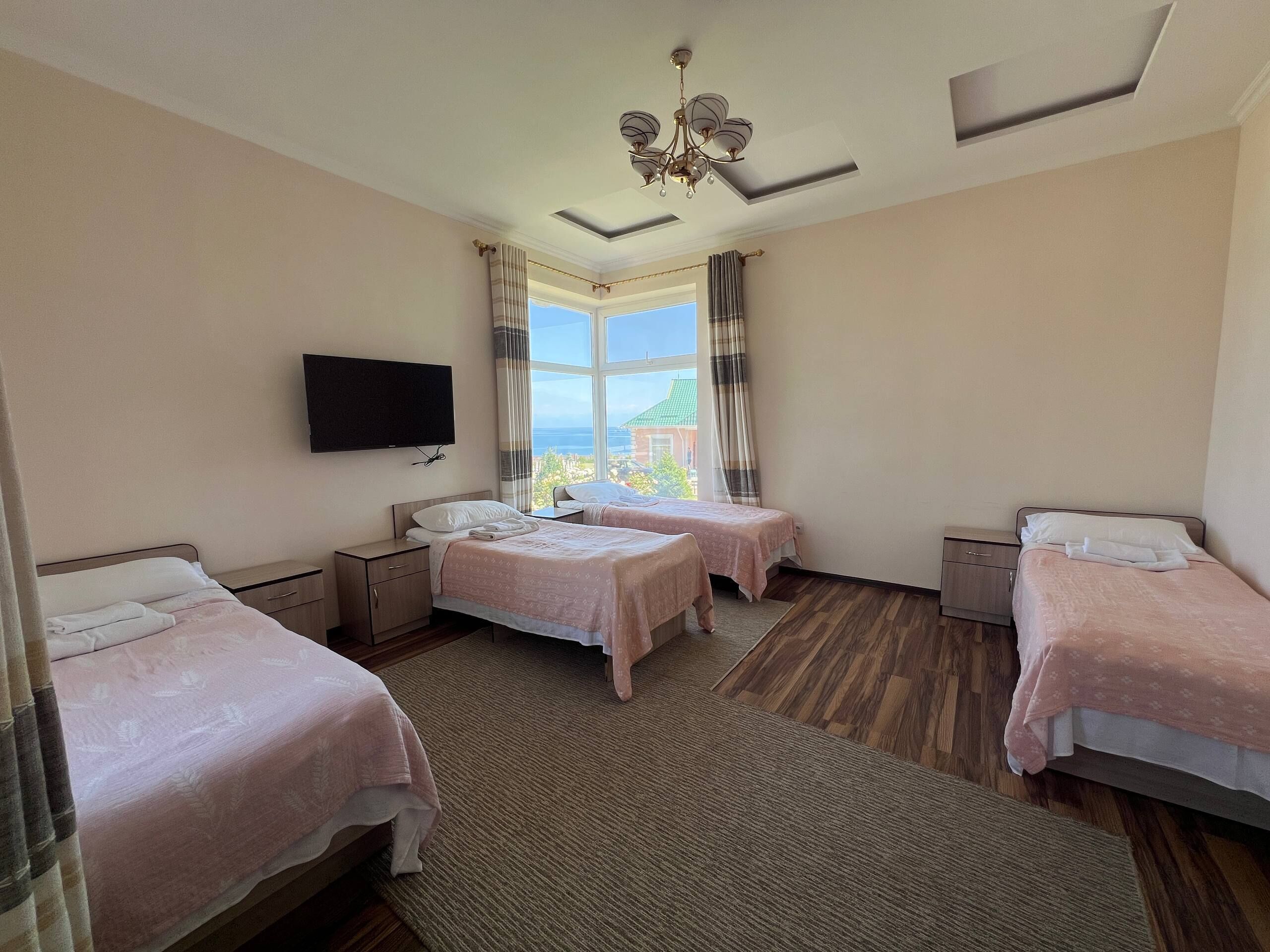 Ein Hotelzimmer mit zwei Betten, einem Flachbildfernseher, einem großen Fenster mit Vorhängen und einer Kristallleuchtre.