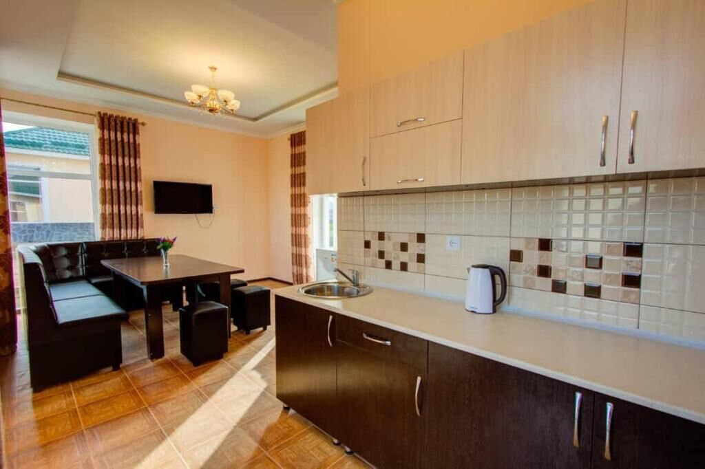 A modern kitchen with dark cabinetry, a tiled backsplash, and a dining area with a table and chairs.