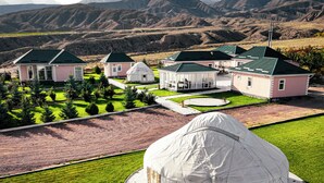 A large white tent-like structure with a patterned base, surrounded by a well-maintained lawn and a building complex with multiple houses.